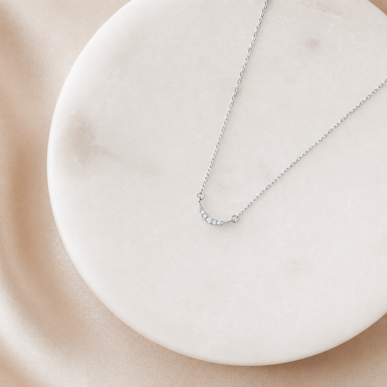 Silver necklace on a white plate with a beige background